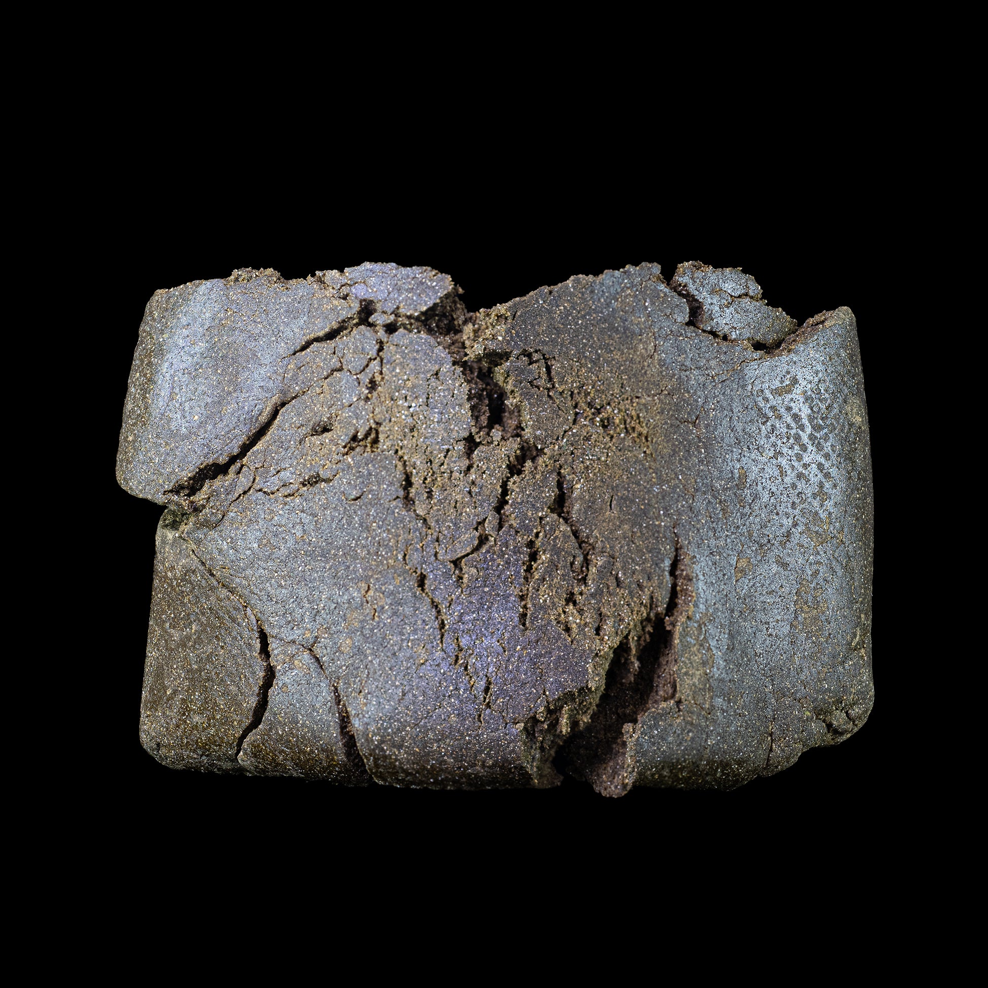 Et helt stykke Manali Hash i pladeform med knækkede og ujævne kanter. Den mørke, næsten sorte farve brydes af lilla og gyldne reflekser i overfladen, hvilket understreger dens klassiske udtryk og tætte, olierede struktur.